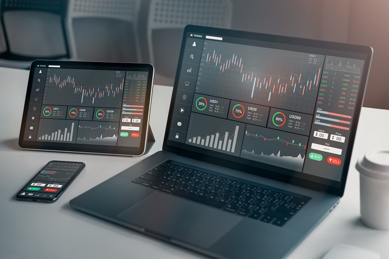 Ein schwarzer Latop, ein Tablet und ein Mobiltelefon auf einem Tisch mit einer Kaffeetasse und einer Maus, auf dem Börsencharts und Daten zur Datenanalyse zu sehen sind